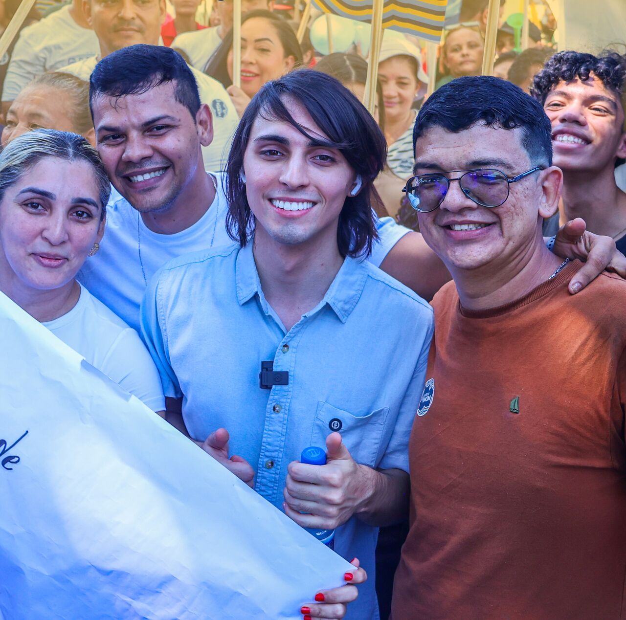 Amom Mandel abraçado a apoiadores em um ato de rua, com cartazes da campanha ao fundo